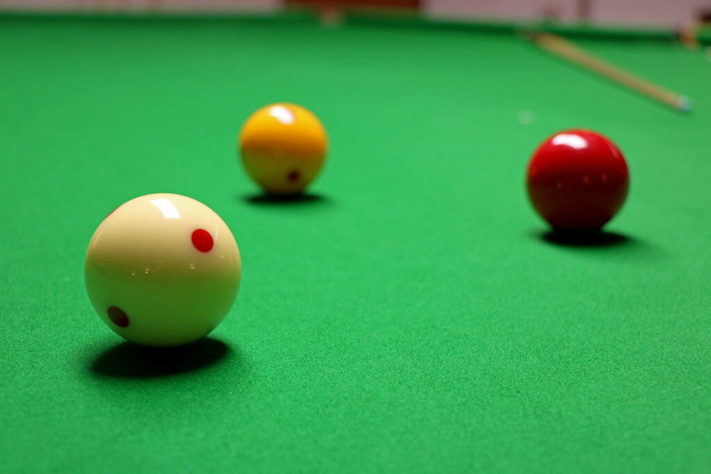 Three billiard balls on green pool table with focused lighting and cue stick in background wallpaper
