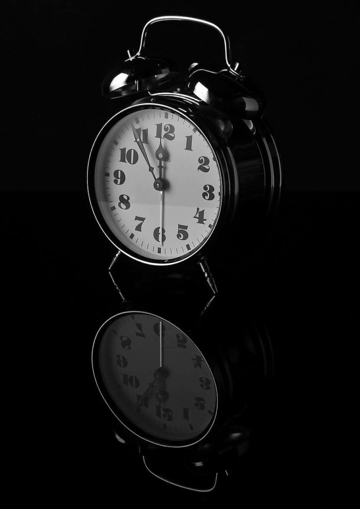 Classic black alarm clock with white dial reflected on glossy black surface minimalist design wallpaper