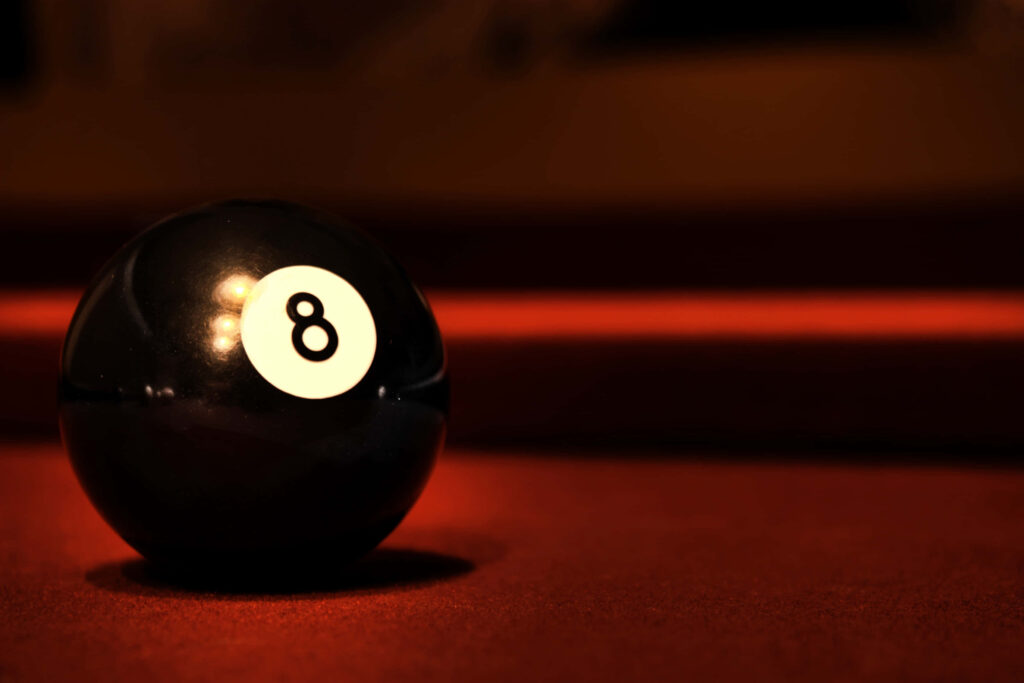 Close-up of glossy black eight ball on red pool table with warm moody lighting background Wallpaper