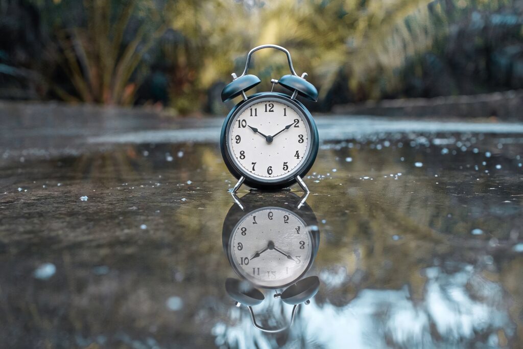 Classic blue alarm clock on wet reflective surface with blurred nature background and sharp focus Wallpaper