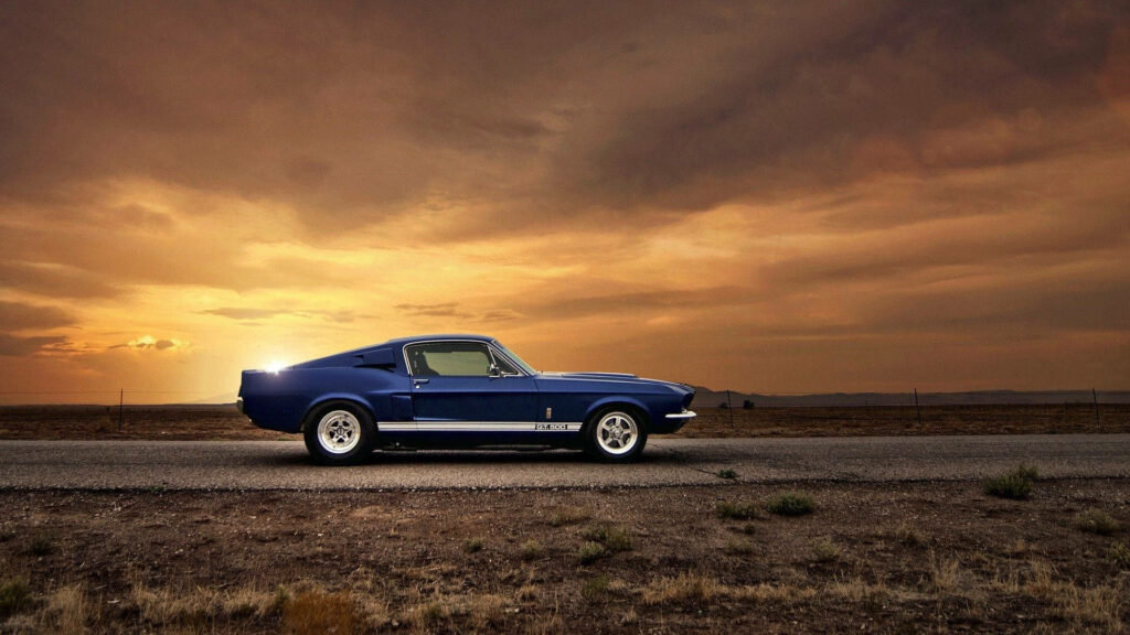 Classic blue muscle car driving on open road at sunset with dramatic golden sky background Wallpaper