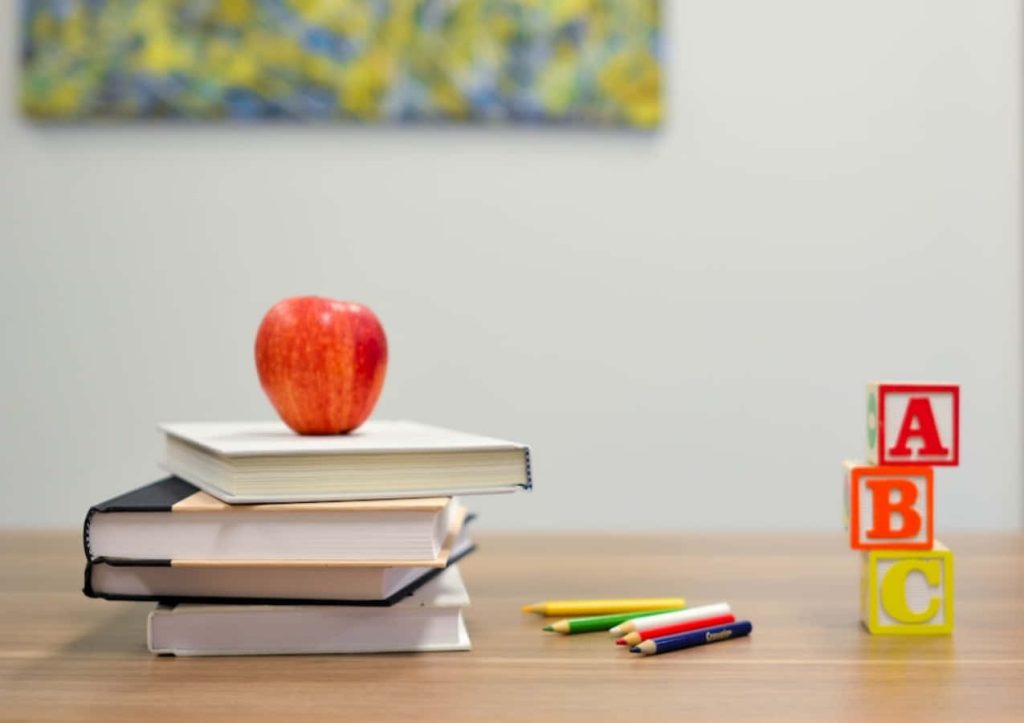 Stack of books with red apple colorful pencils and ABC blocks on wooden table learning wallpaper