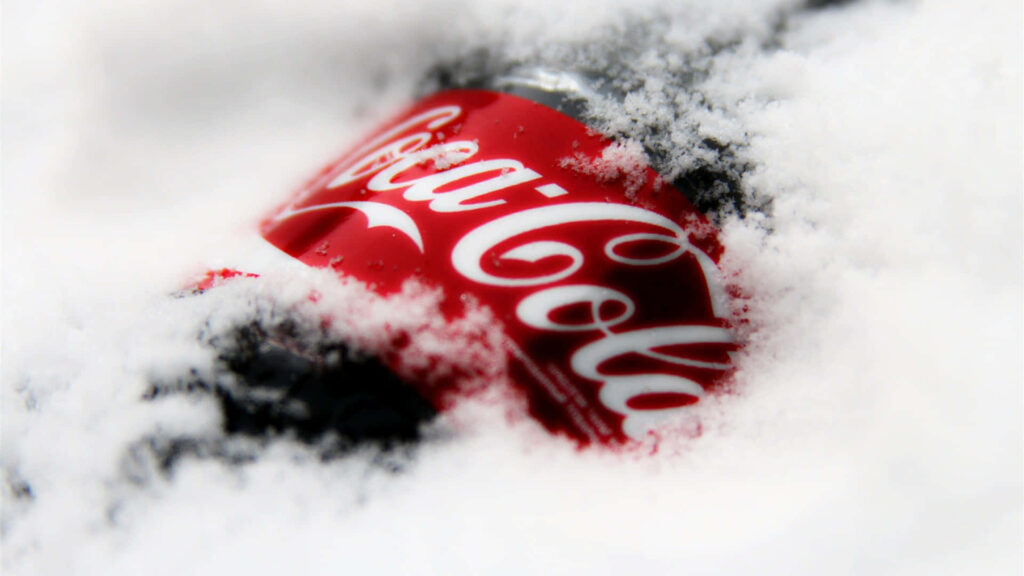 Classic Coca Cola bottle in fresh white snow with vibrant red label creating cool refreshing vibe Wallpaper