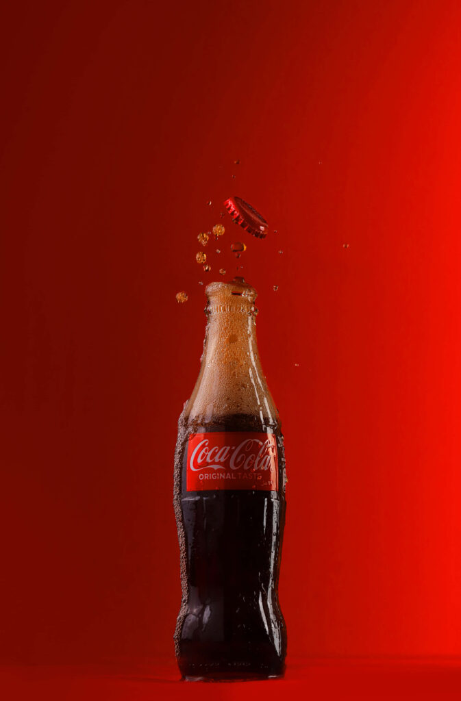 Classic Coca-Cola bottle with bubbles rising and cap popping off on vibrant red background wallpaper