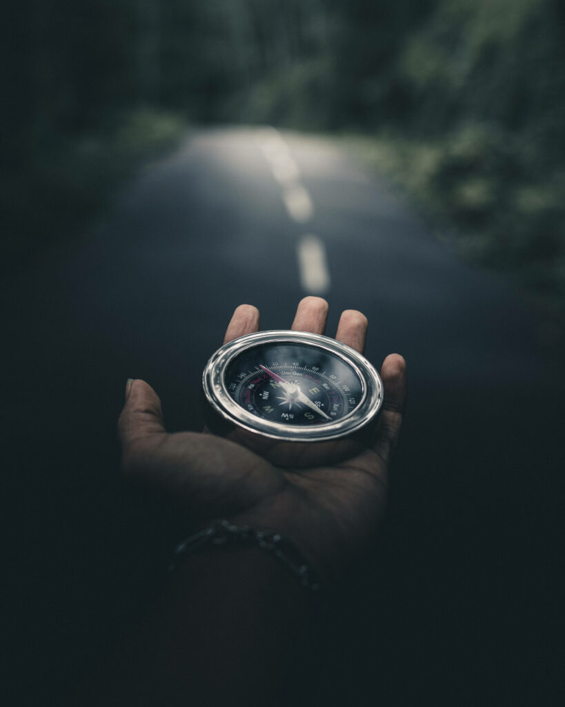 Hand holding classic compass with blurred winding forest road dark moody adventure background Wallpaper