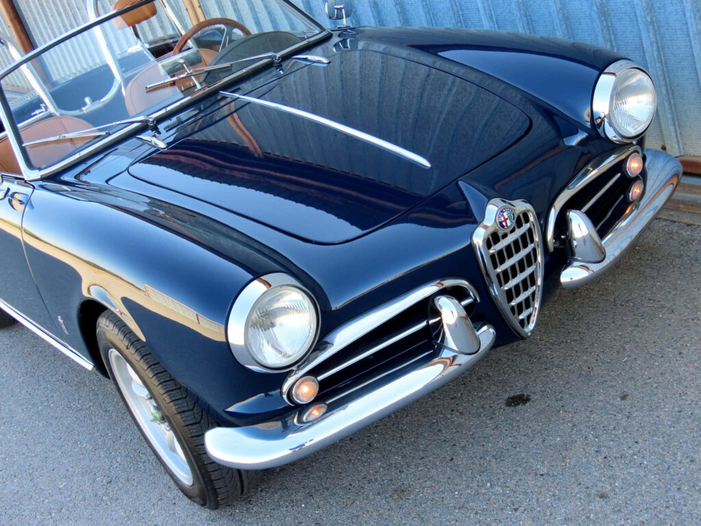 Classic deep blue Alfa Romeo Spider vintage convertible with chrome grille on scenic outdoor drive Wallpaper