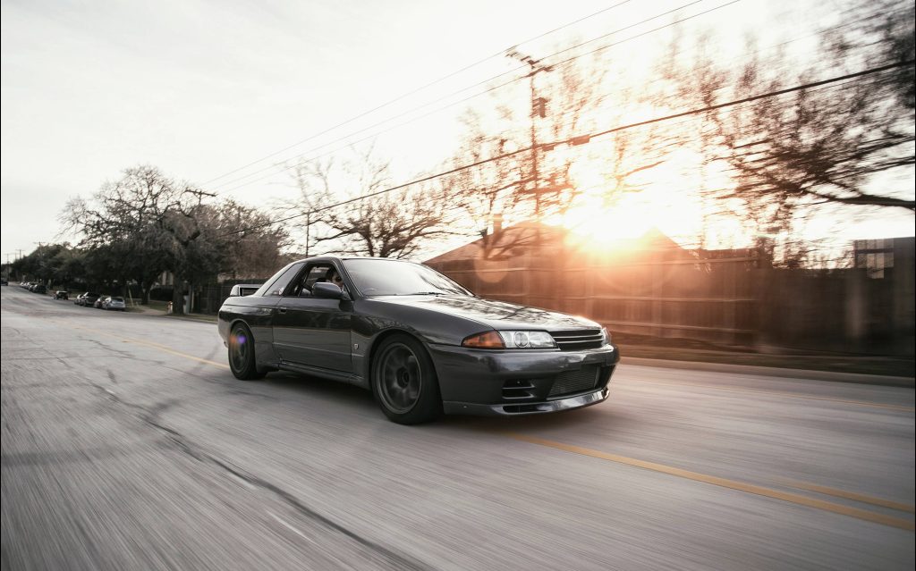 Grey Nissan Skyline GT-R R32 driving at sunset with motion blur on suburban road wallpaper