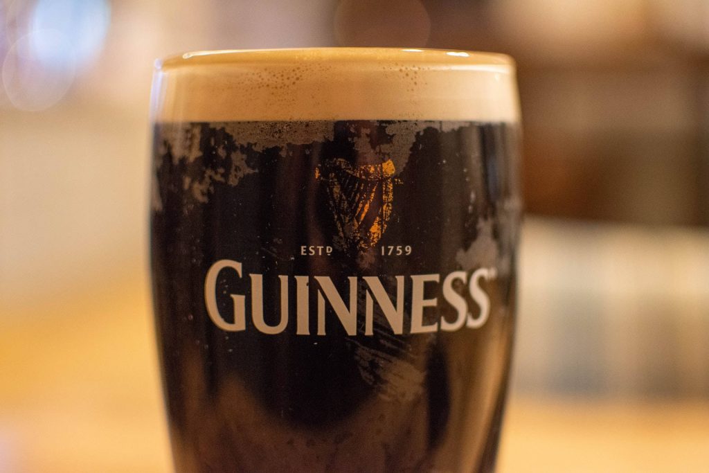 Close-up of classic Guinness Irish Dry Stout with creamy head and warm pub lighting background Wallpaper