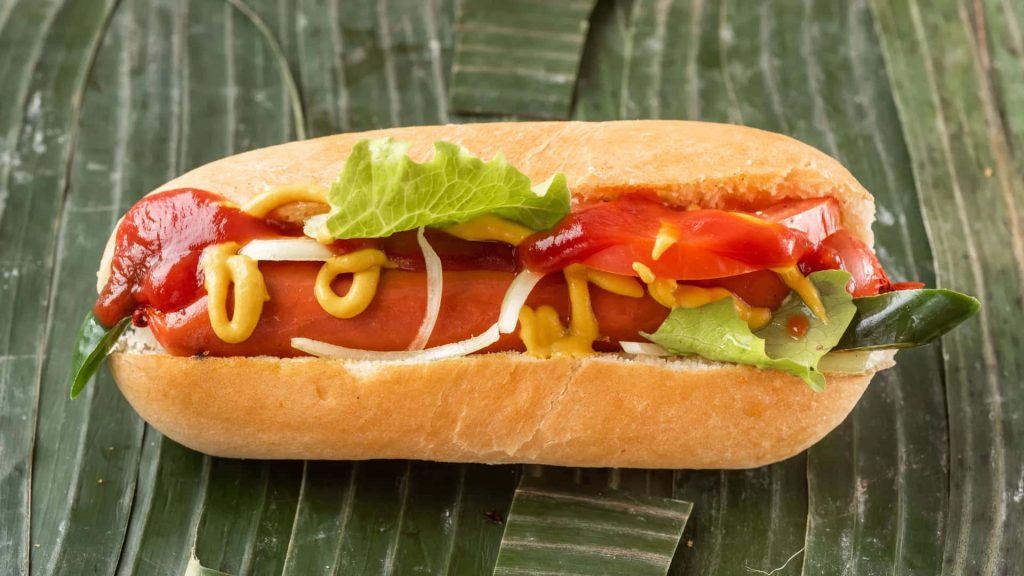 Close-up of a classic hot dog with ketchup mustard lettuce tomato on rustic banana leaf background Wallpaper