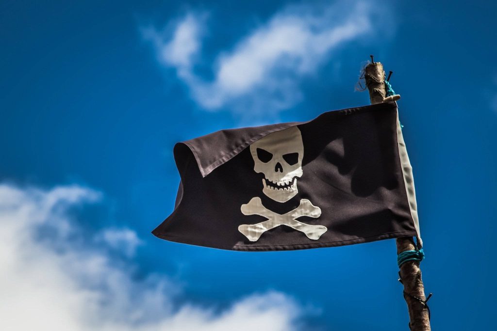 Jolly Roger pirate flag with skull crossbones waving on wooden mast against blue sky background Wallpaper