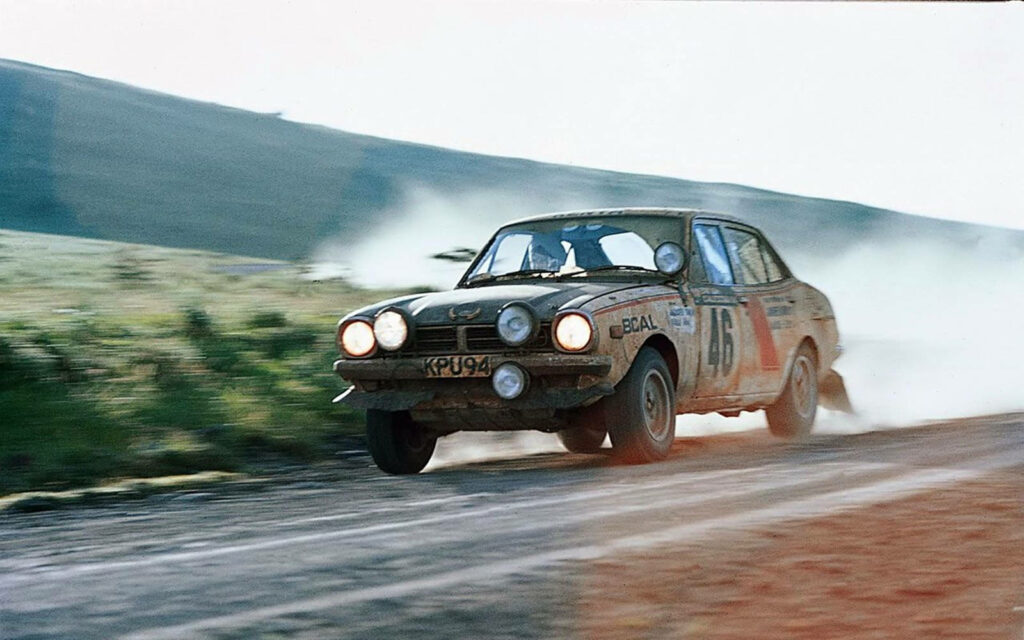 Vintage Mitsubishi Colt Lancer rally car speeding on dusty countryside track in pristine condition Wallpaper