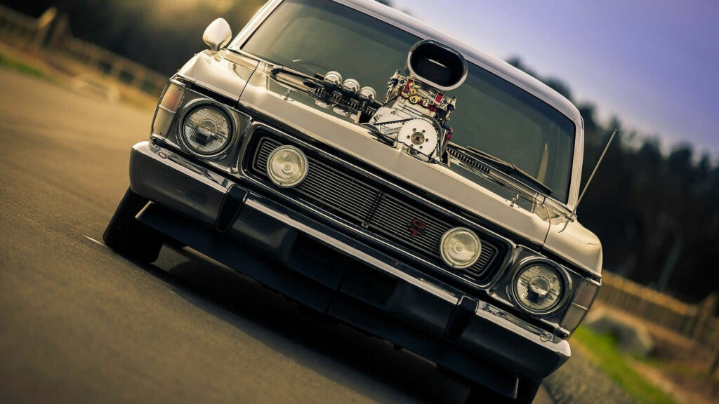 Classic muscle car with exposed engine and chrome details on open road high-speed racing wallpaper