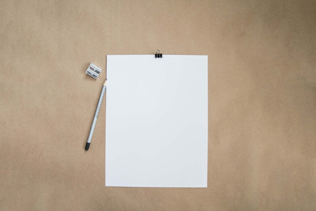 Stationery Essentials: Blank White Paper and Clip on Brown Surface Wallpaper