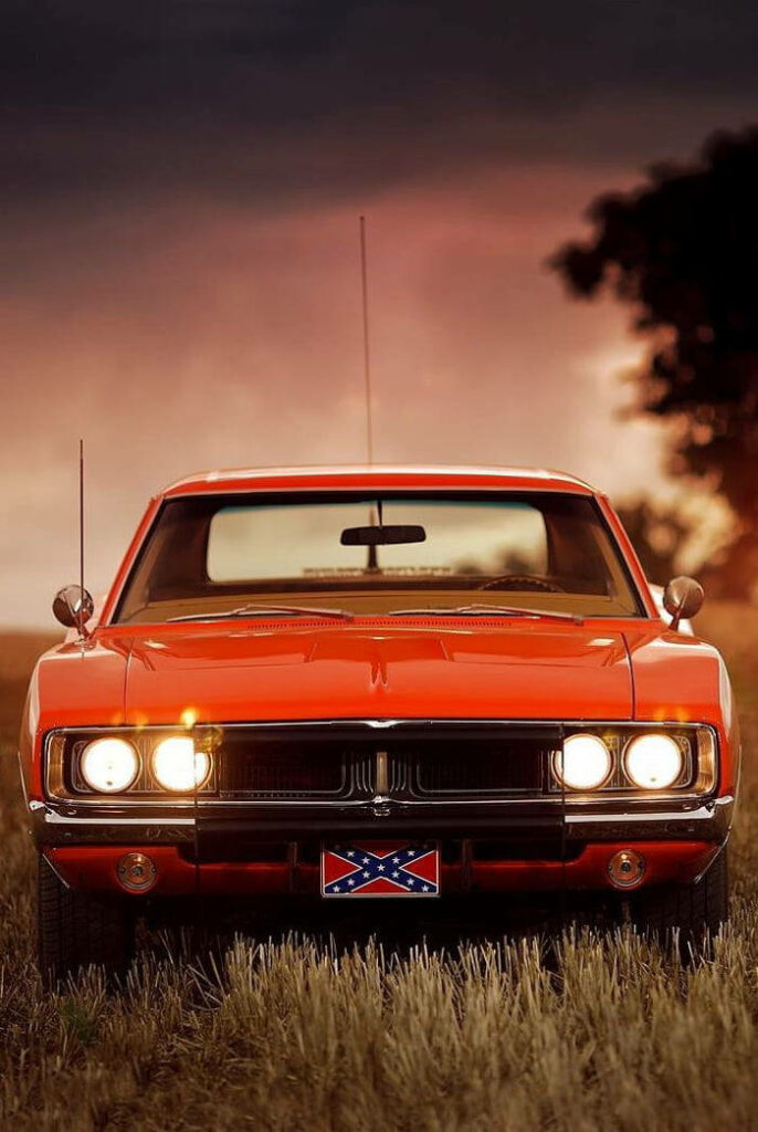 Classic orange General Lee car parked in grassy field under vibrant sunset sky nostalgic scene Wallpaper