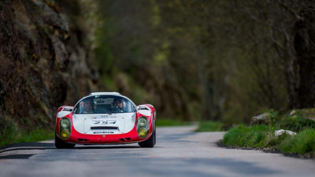 Classic Porsche 906 racing on winding road with lush greenery and rocky cliffs vintage car wallpaper