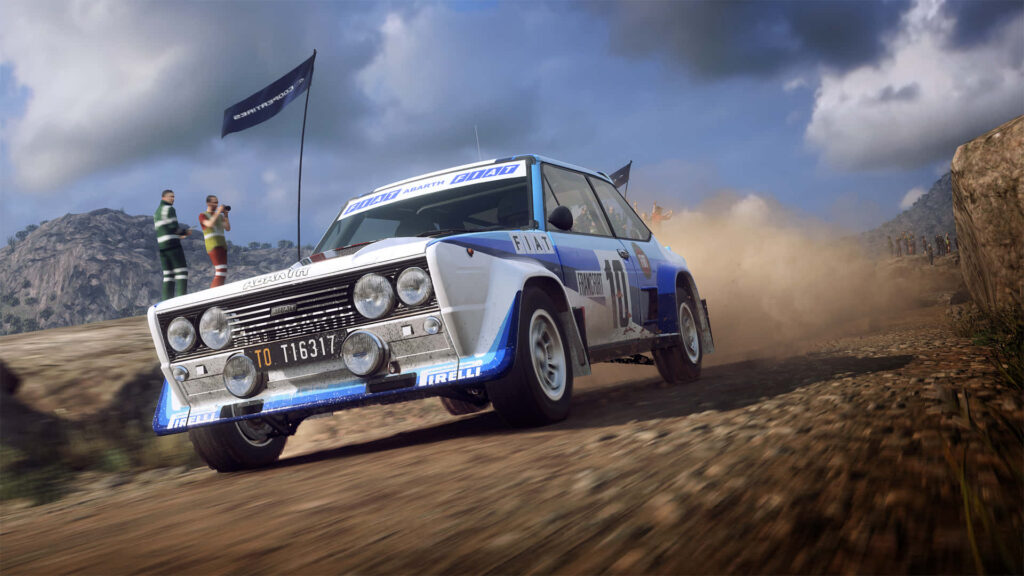 Classic rally car racing on dusty off-road track kicking up dirt against rugged landscape wallpaper