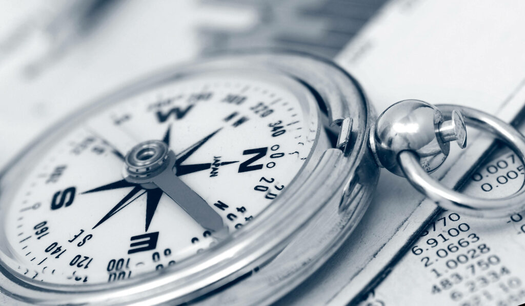 Close-up of classic silver compass with white dial and black markers on gray blurred background Wallpaper