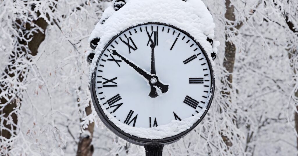 Classic round clock covered in thick snow with frosty trees winter wallpaper background