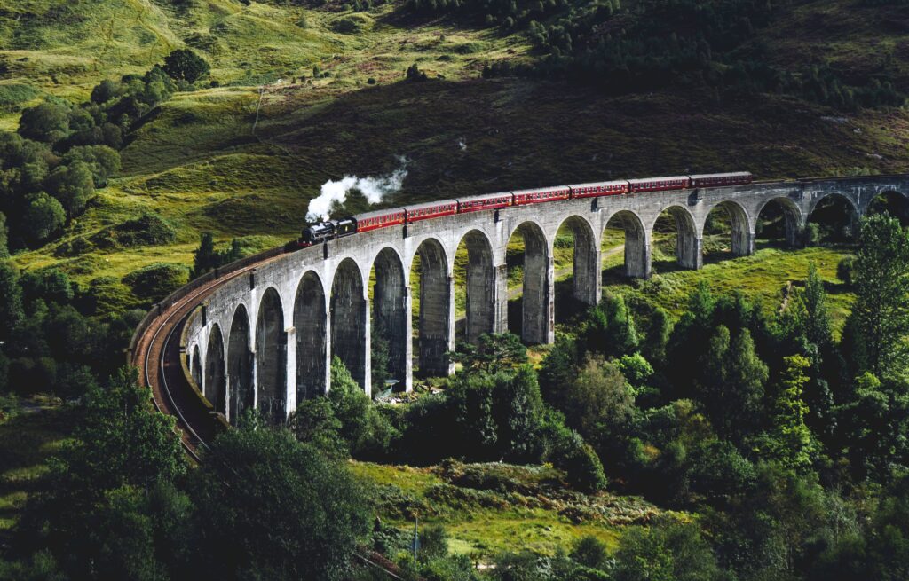 Classic steam train crossing stone bridge lush green hills sunlight landscape wallpaper