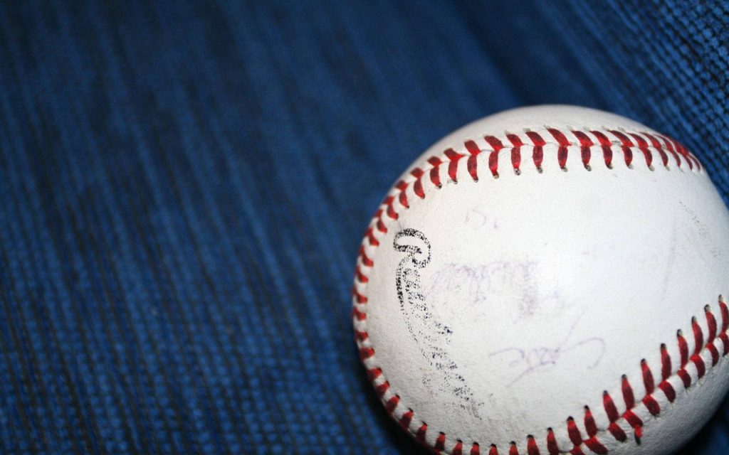 Classic white baseball with red stitching on blue carpet minimalist sporty wallpaper background