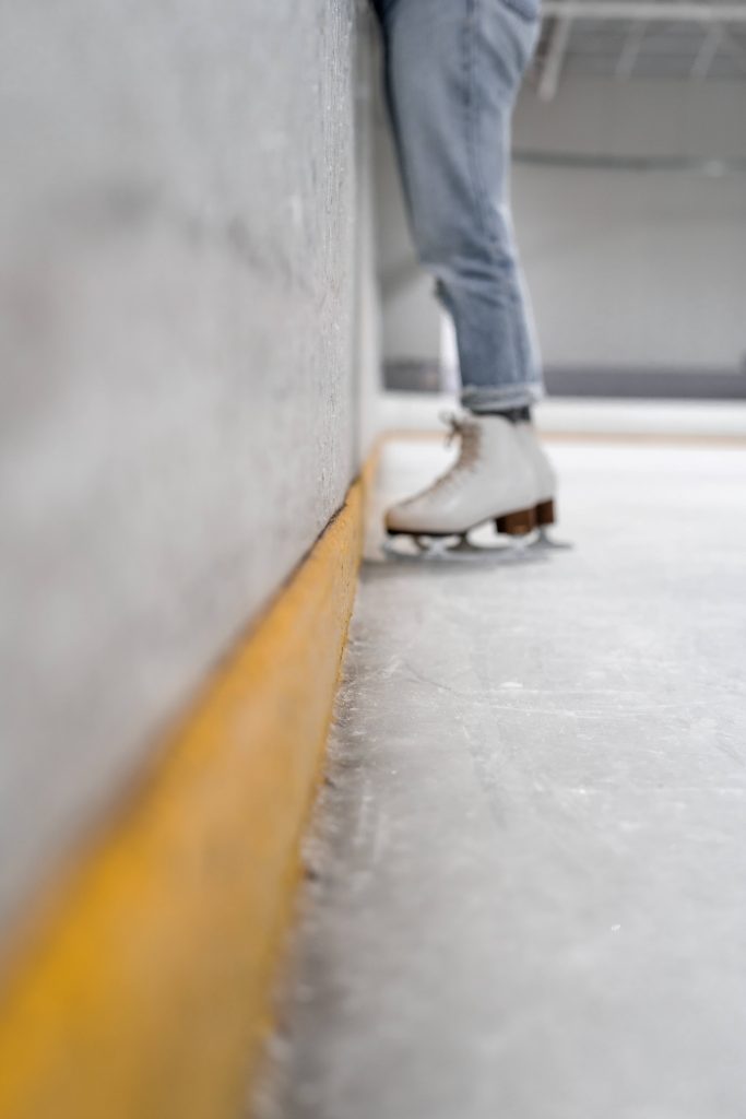 Classic white figure skates on ice rink with skater in jeans near yellow-trimmed wall 4K wallpaper