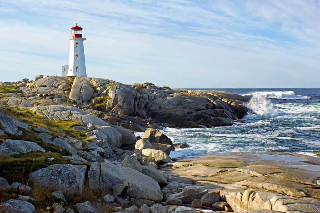 Classic white lighthouse on rocky coast with deep blue sea waves under serene sky wallpaper