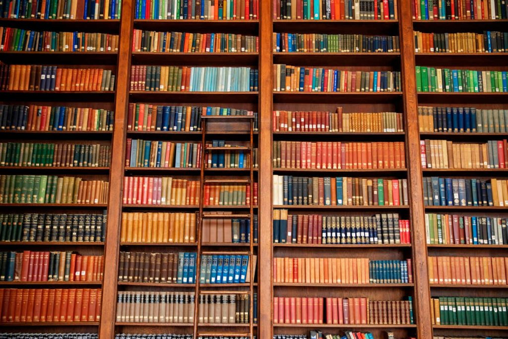 High resolution floor to ceiling wooden bookshelf with library ladder colorful book spines background Wallpaper