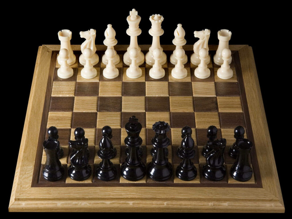 Classic wooden chessboard with black and white pieces set for game start on dark background Wallpaper