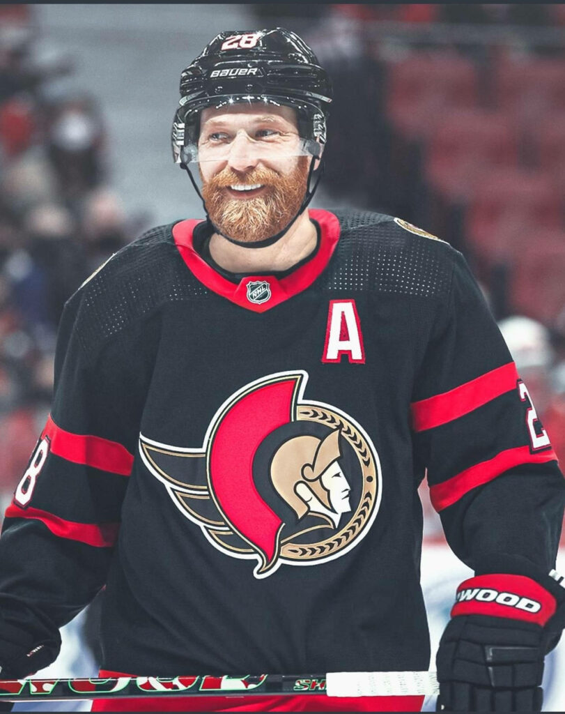 Claude Giroux smiling in Ottawa Senators jersey black red gold in dynamic hockey arena background Wallpaper