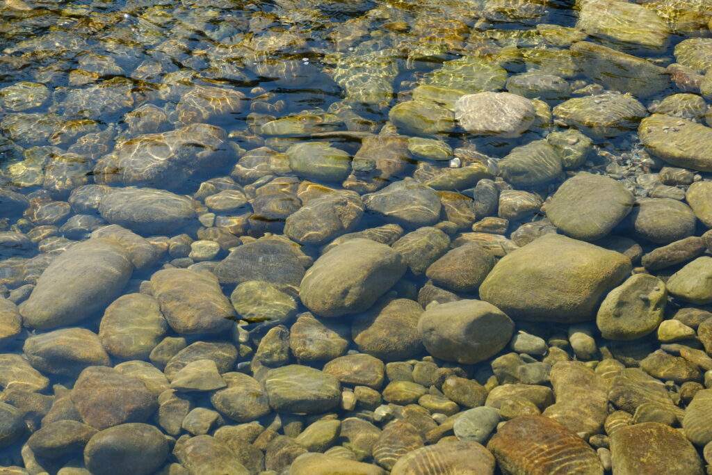 Smooth rounded stones beneath clear water with sunlight reflections serene natural wallpaper