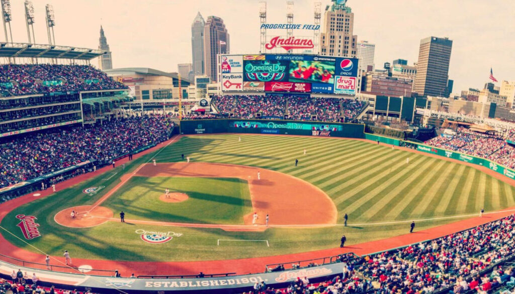 Packed Progressive Field at Cleveland Indians game with players green grass and city skyline Wallpaper