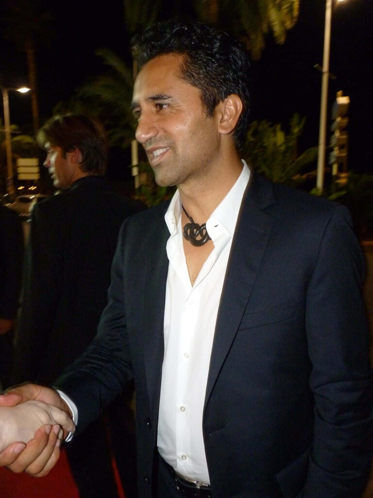 Cliff Curtis in black suit on red carpet with palm trees and dim lighting elegant event background Wallpaper