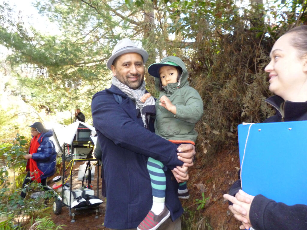 Cliff Curtis holding child outdoors forest film set behind scenes natural lighting green tones Wallpaper