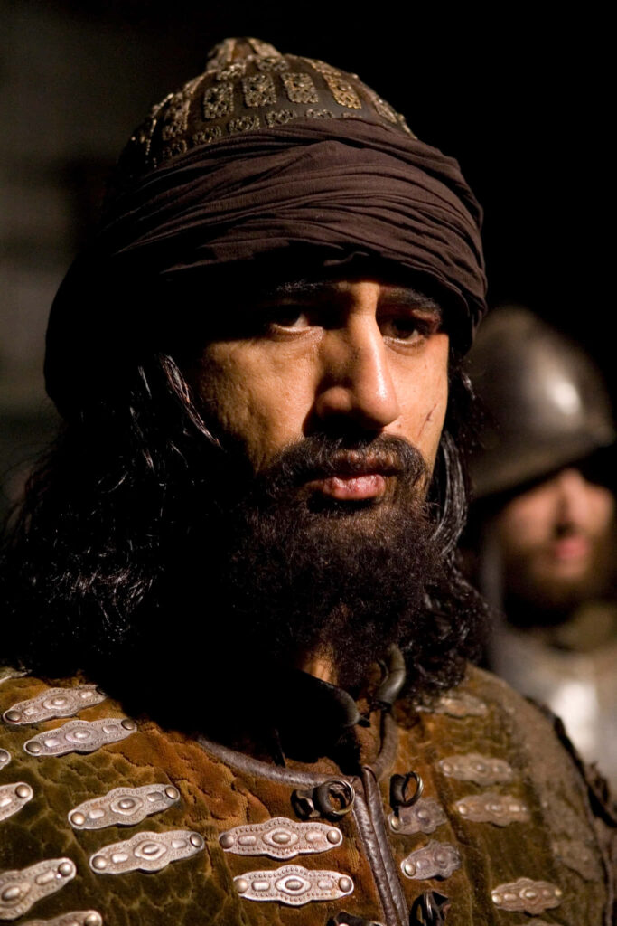 Cliff Curtis as medieval warrior in detailed armor and headpiece against shadowed ancient backdrop Wallpaper
