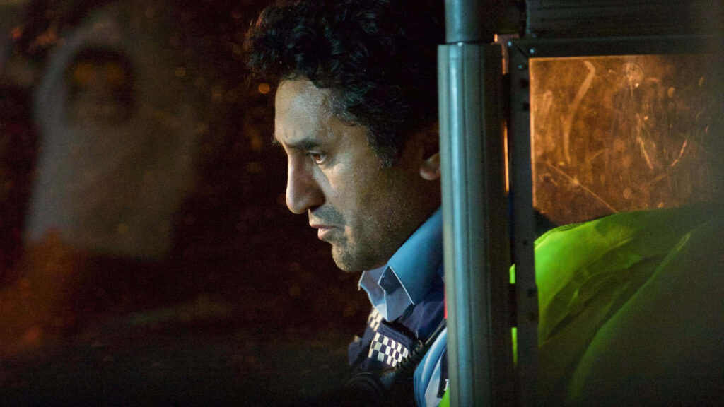 Cliff Curtis in police uniform with intense expression moody lighting blurred urban background wallpaper