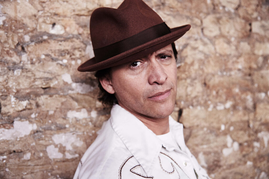 Clifton Collins Jr candid portrait brown fedora white embroidered shirt rustic stone wall background Wallpaper
