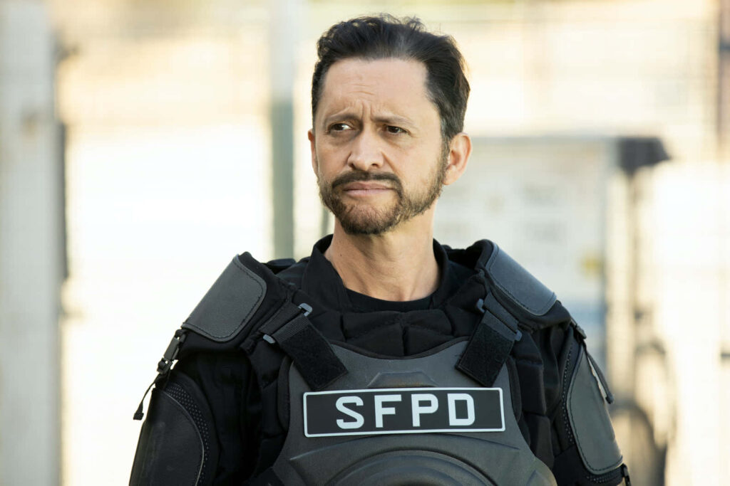 Clifton Collins Jr in sunlit urban SWAT gear with SFPD vest focused on law enforcement duty Wallpaper