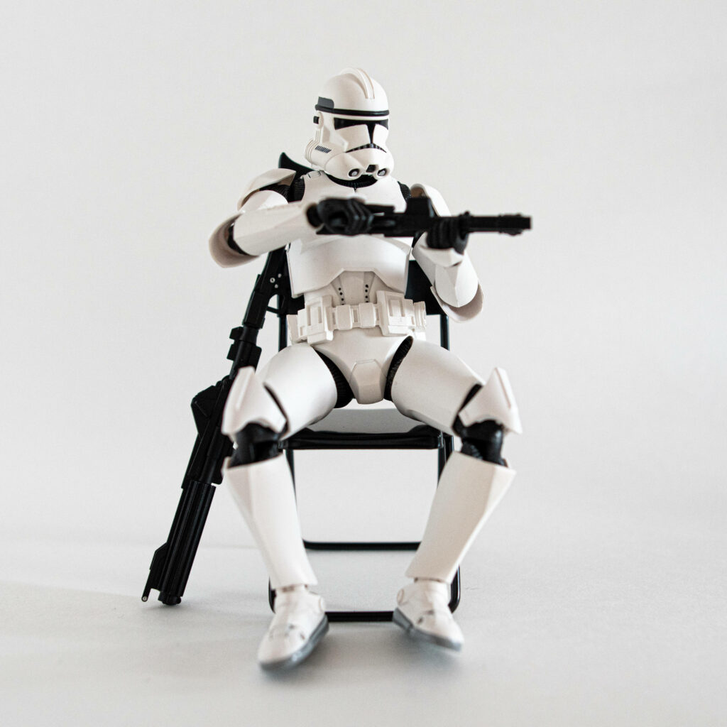 Clone Trooper action figure in white armor holding blaster on black chair minimal white background Wallpaper