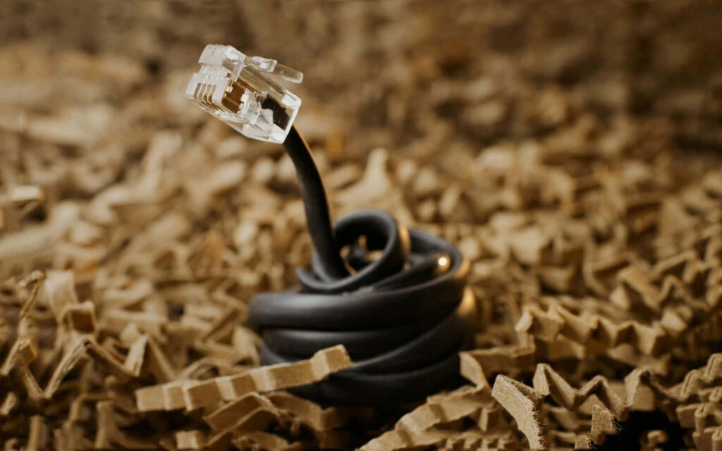 Close-up of black Ethernet cable connector coiled on shredded brown paper with warm lighting Wallpaper