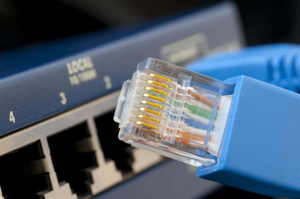 Close-up of blue Ethernet cable with clear RJ45 connector and gold contacts on network switch Wallpaper