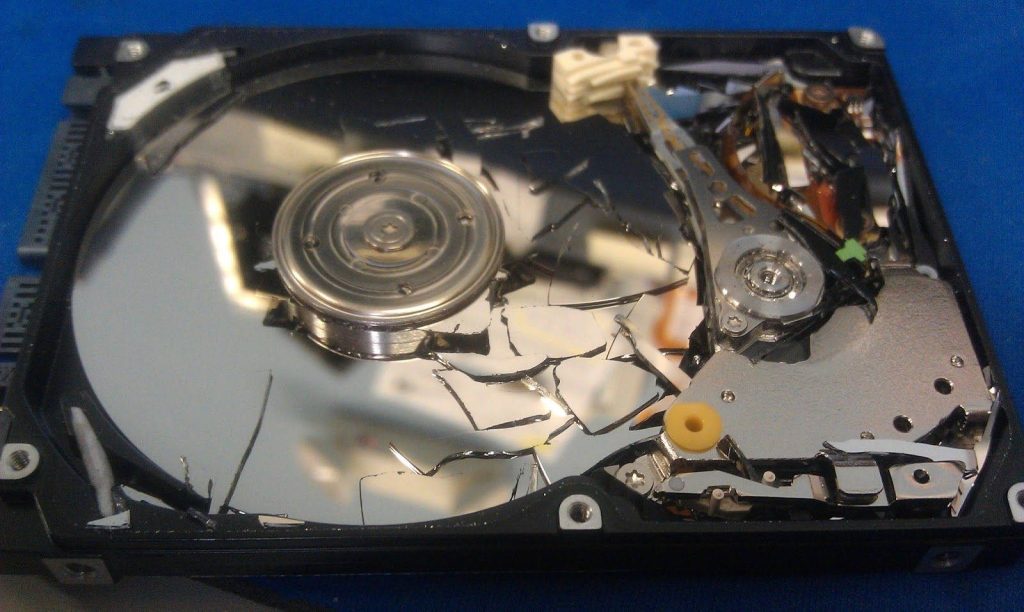 Close-up of shattered hard drive platter showing actuator arm and spindle motor on blue background Wallpaper