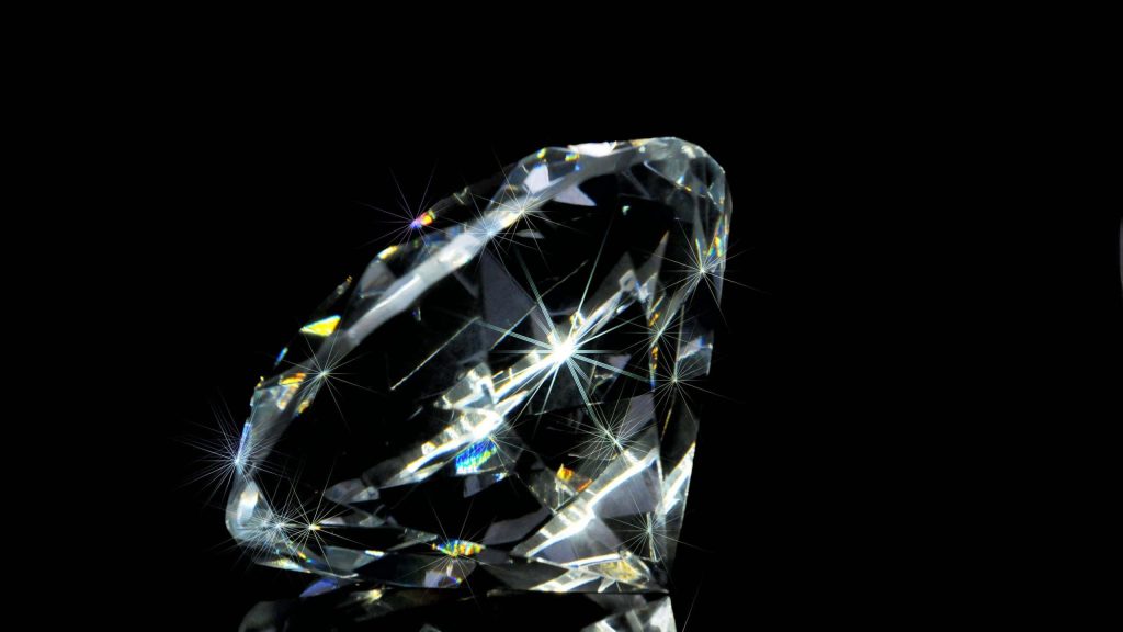 Close-up image of sparkling diamond with starburst light flares on black aesthetic wallpaper background