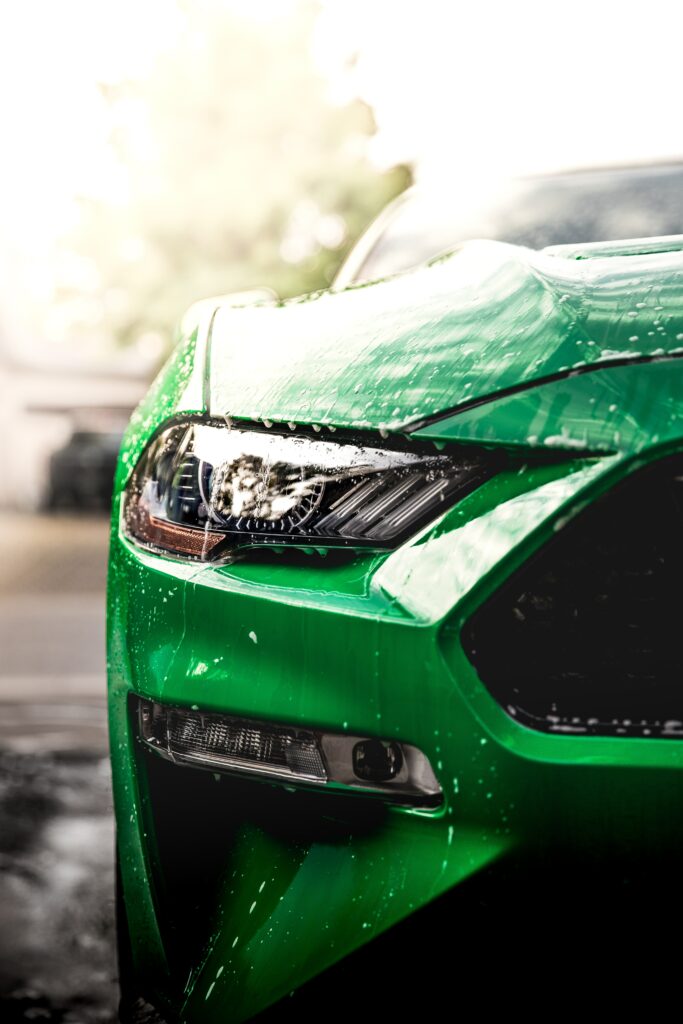 Sleek Green Car Close-Up: Illuminated Headlight & Wet Surface Wallpaper