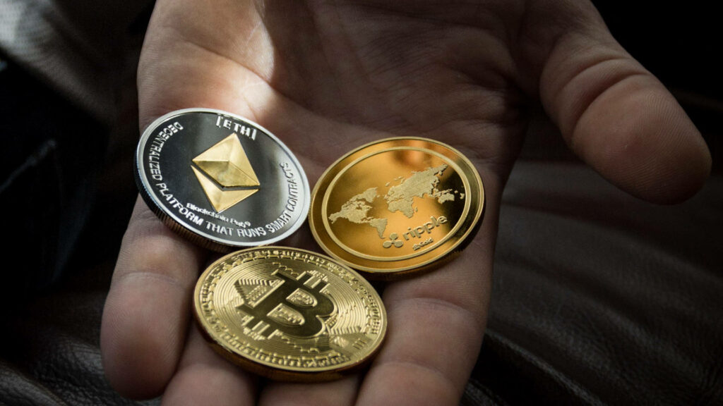 Hand holding three glossy Ethereum Bitcoin Ripple coins symbolizing digital currency blockchain tech Wallpaper