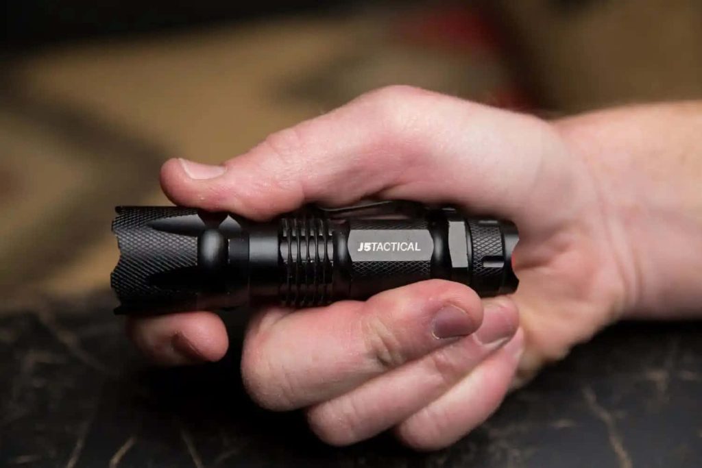 Hand gripping rugged black J5 Tactical flashlight with metallic finish minimalist wallpaper background