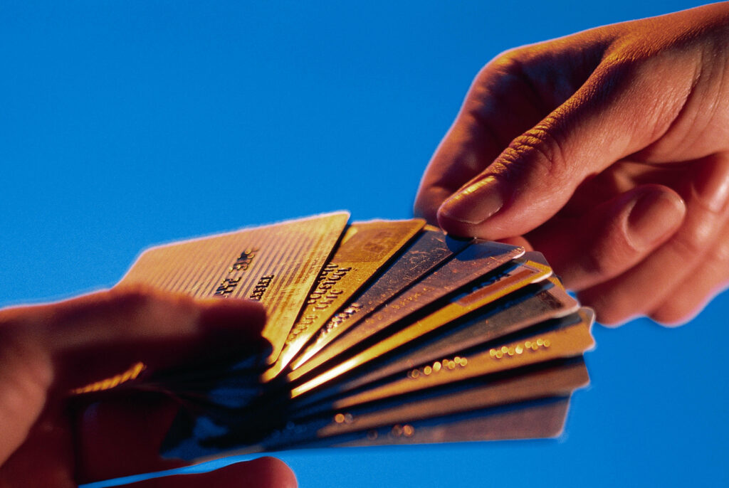 Two hands exchanging shiny credit cards on vibrant blue background symbolizing modern finance. Wallpaper