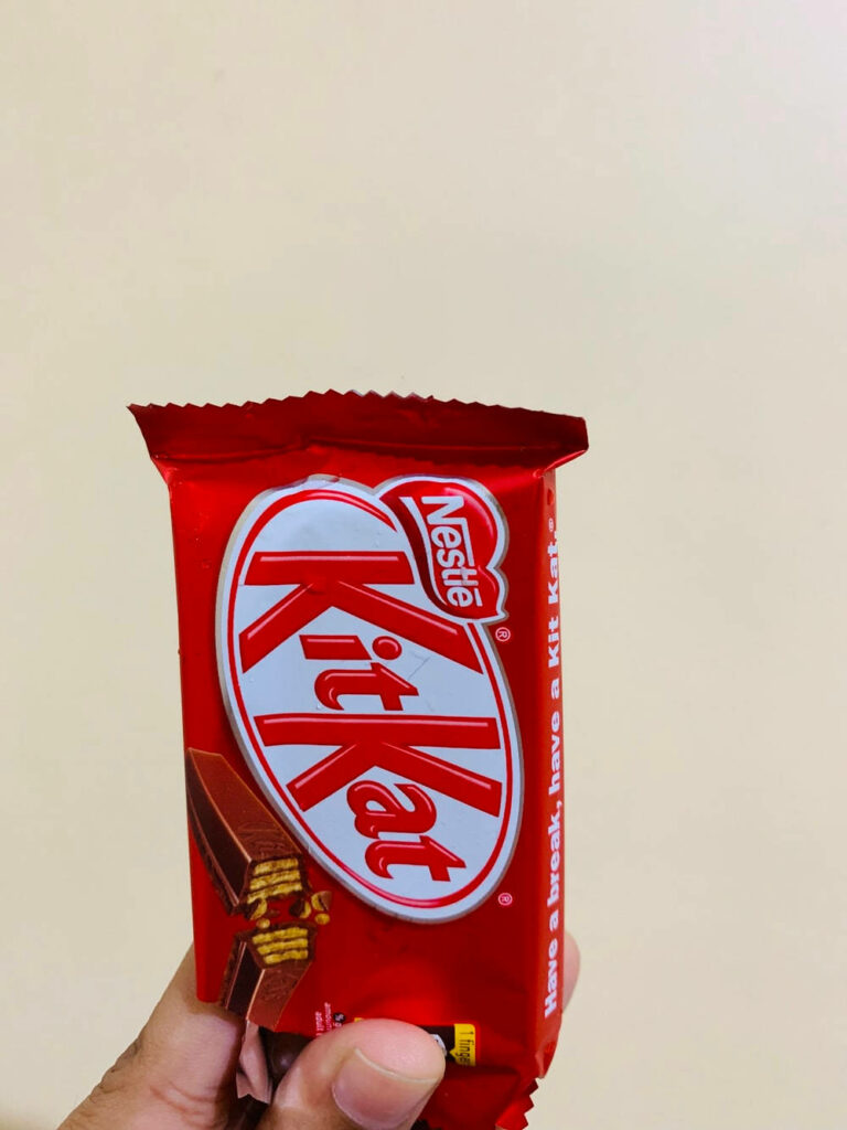 Hand holding red Kit Kat wrapper close up vibrant chocolate bar branding on beige background Wallpaper
