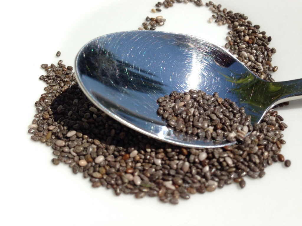Close-up of shiny metallic spoon resting on textured chia seeds on white surface wallpaper background