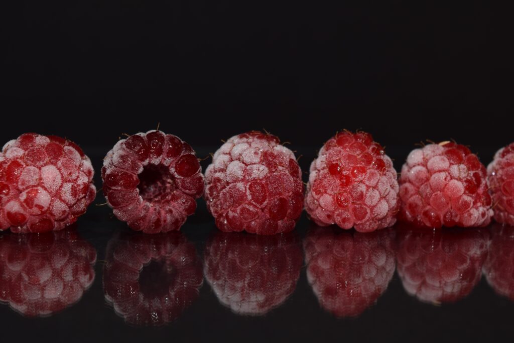 Close-Up of Frozen Raspberries: Vibrant Red on Reflective Black Background Wallpaper