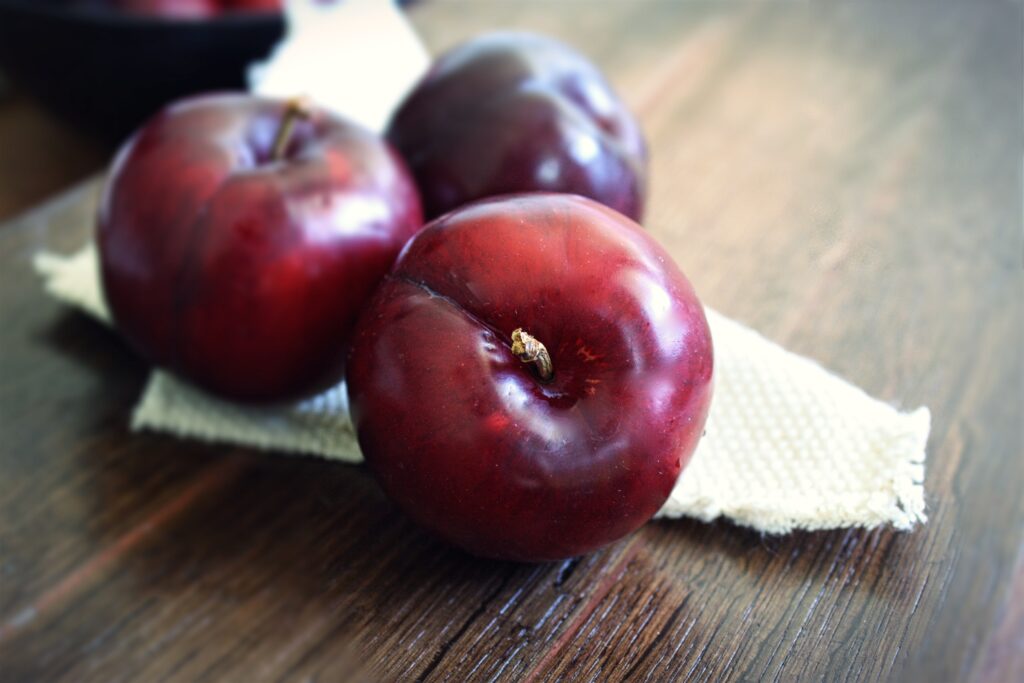 Ripe Red Plums Close-Up: Juicy Wallpaper Background on Wood